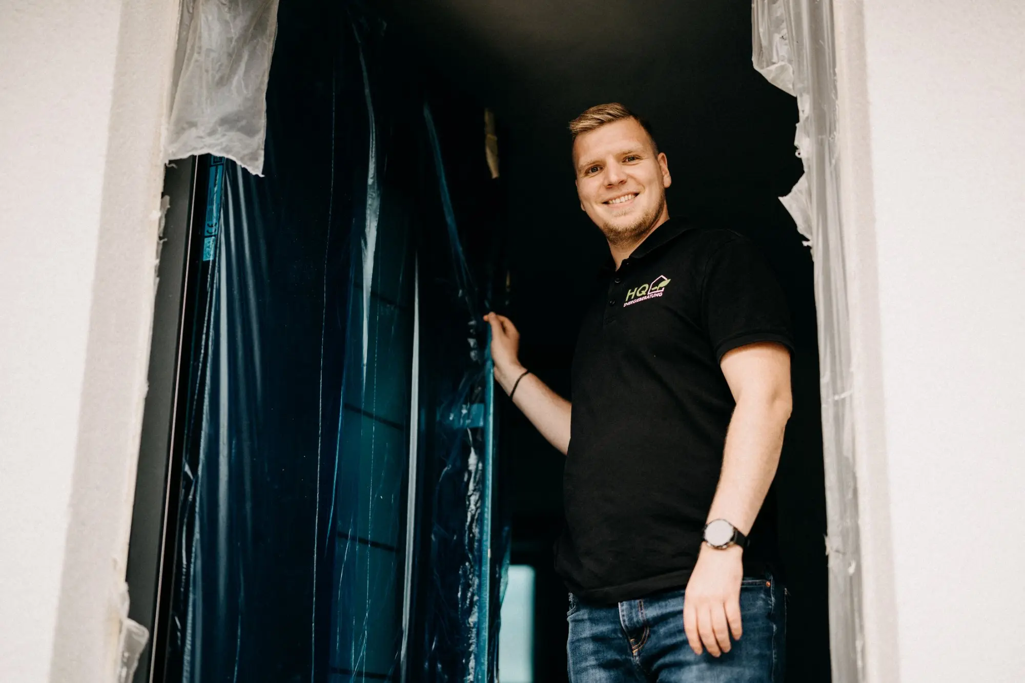 Andre Handschuh von HQ Energieberatung steht lächelnd auf einer Baustelle neben einer Fensteröffnung mit Schutzfolie