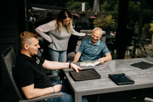 Andre Handschuh von HQ Energieberatung berät ein Kundenpaar auf der Terrasse – Frau schaut interessiert auf die Broschüre