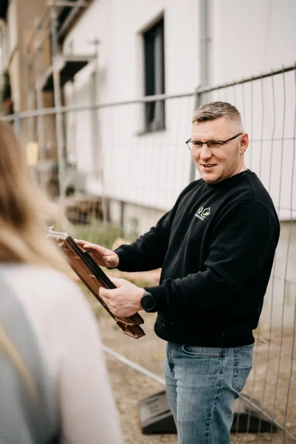 Florian Handschuh von HQ Energieberatung zeigt einer Kundin Unterlagen bei einer Vor-Ort-Beratung am Gebäude
