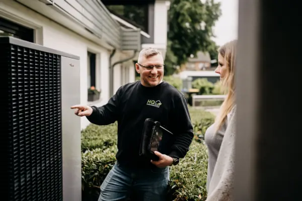 Florian Handschuh von HQ Energieberatung erklärt einer Kundin die Funktionsweise einer Wärmepumpe am Wohnhaus